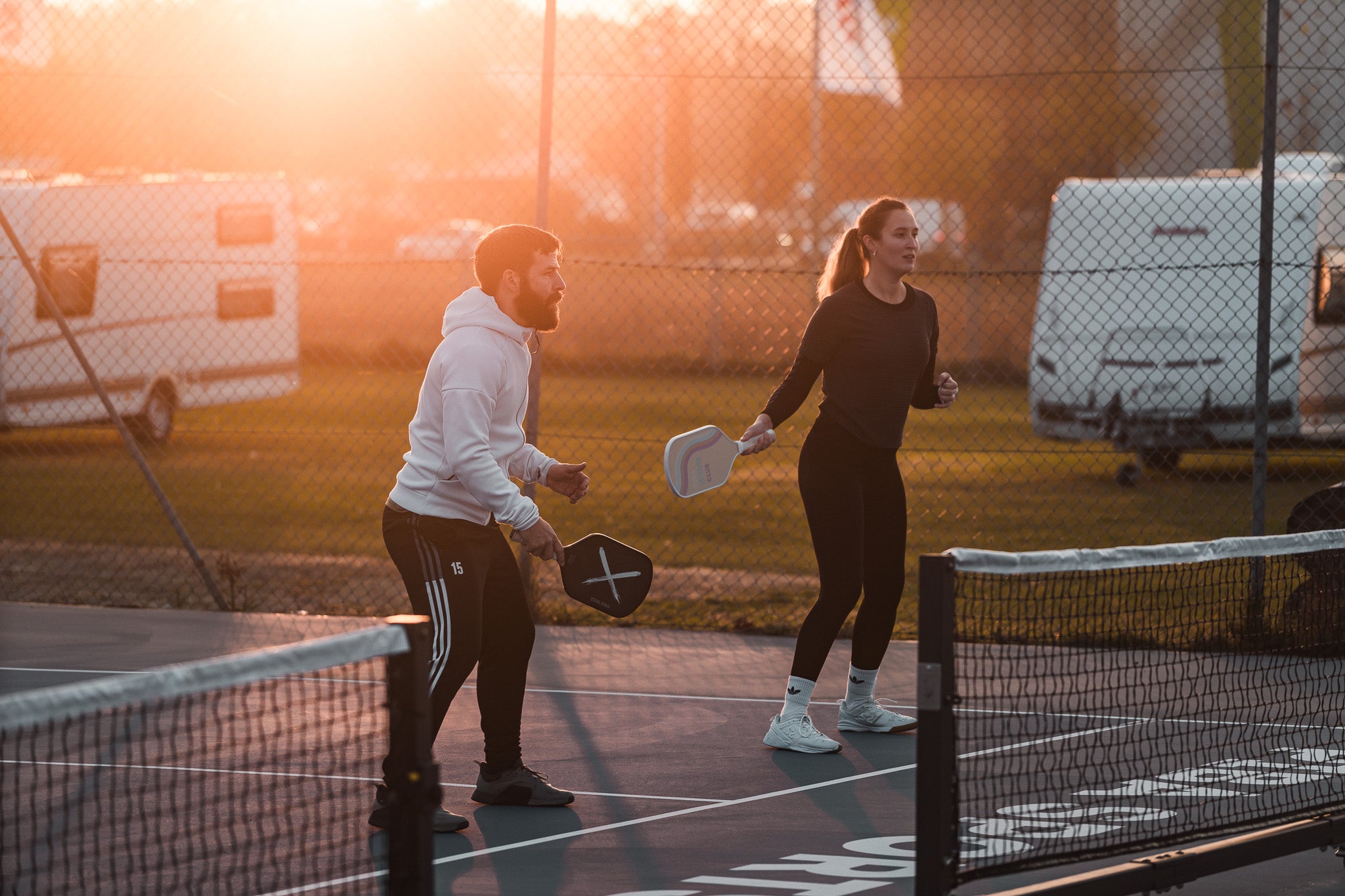 Mann und Frau spielen Pickleball bei Sonnenuntergang auf Outdoor Courts von Piba Sports, beide mit Piba Sports Pro Paddles in der Hand