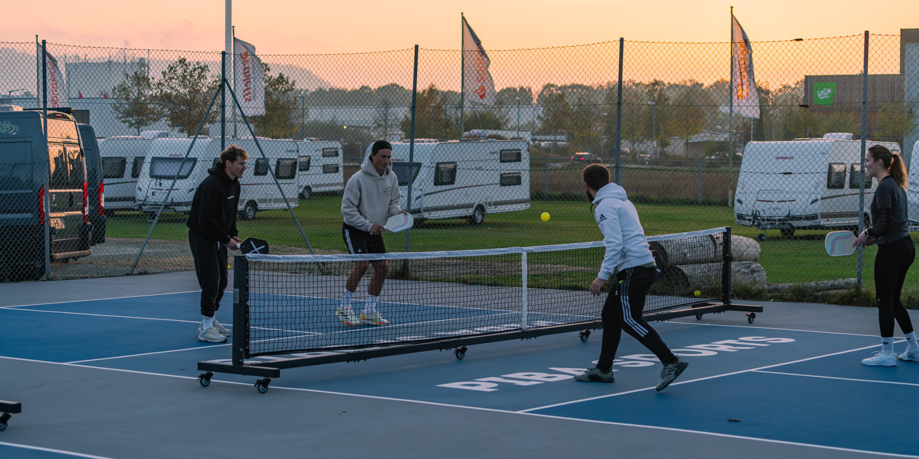 Vier Personen spielen gemeinsam Pickleball mit Piba Sports Schlägern auf einem deutschen Pickleball-Platz, während der Ball über das Piba Sports Pro Netz fliegt – spannendes Match mit hochwertiger Ausrüstung